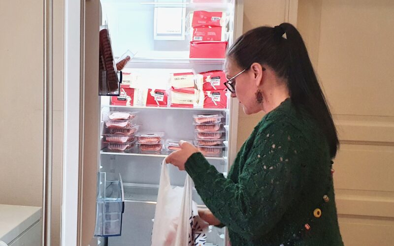 Diakoniatyöntekijä kerää avustuskassiin elintarvikkeita jääkaapista.