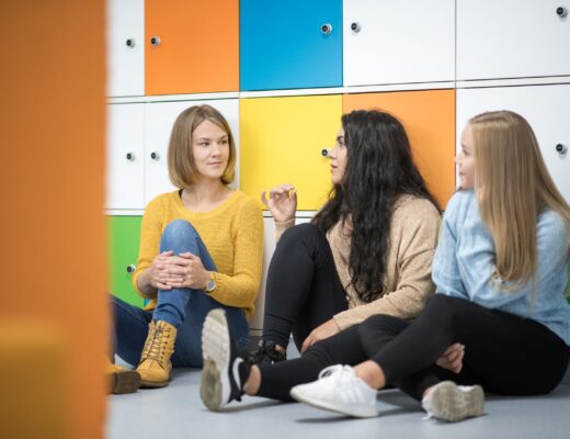 Nuoria naisia istuu lattialla värikkäiden lokerikkojen edessä.