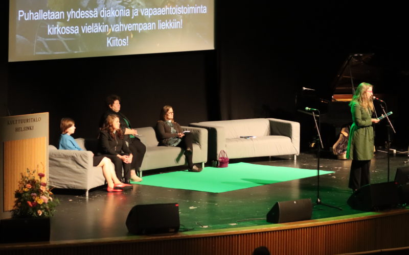 Diakoniabarometrin tutkijat istuvat sohvalla, Titi Gävert puhuu Kulttuuritalon lavalla.