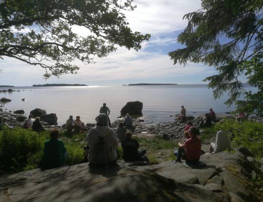 Ihmisiä istuu kallioilla järven rannalla.