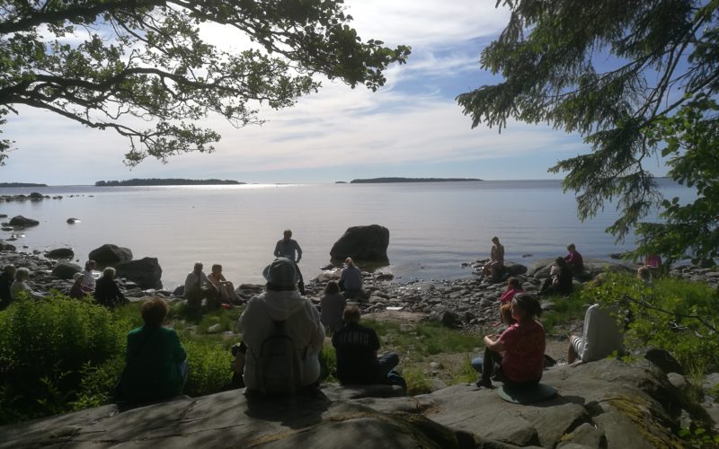 Ihmisiä istuu kallioilla järven rannalla.
