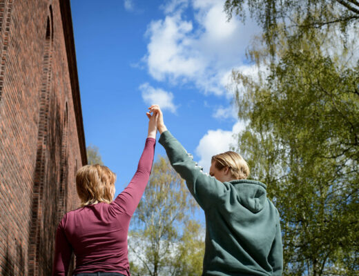 Kaksi nuorta ovat nostaneet yhteenliitetyt kädet ylös onnistumisen merkiksi. He näkyvät kuvassa takaapäin. On kesäinen aurinkoinen päivä.