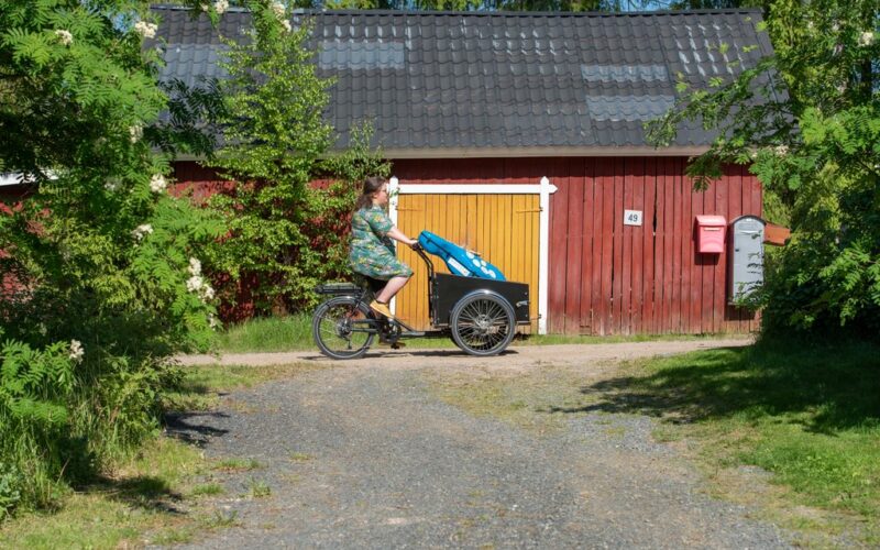Henkilö ajaa sähkötaakkapyörällä maatalon pihapiirissä kesäisenä päivänä.